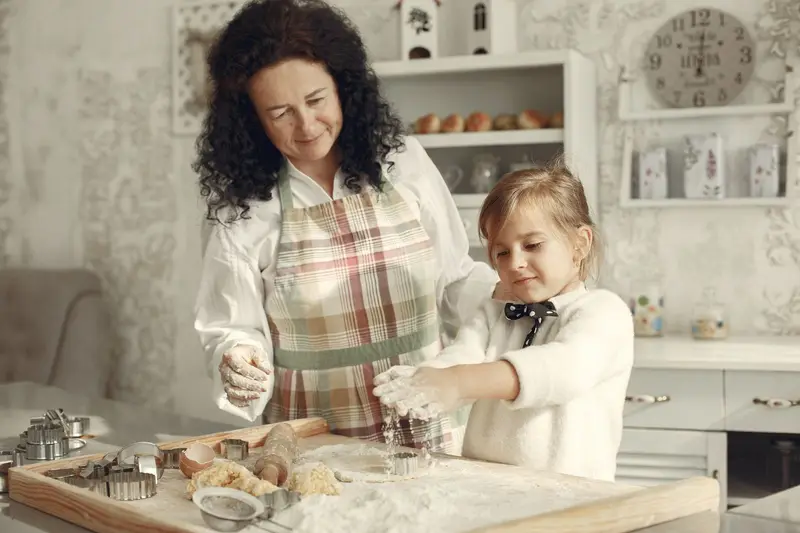 A grandmother and granddaughter make dough together in a cozy kitchen