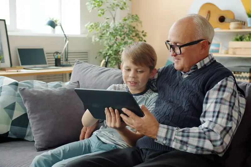 A grandfather and grandson look at a tablet together on the couch